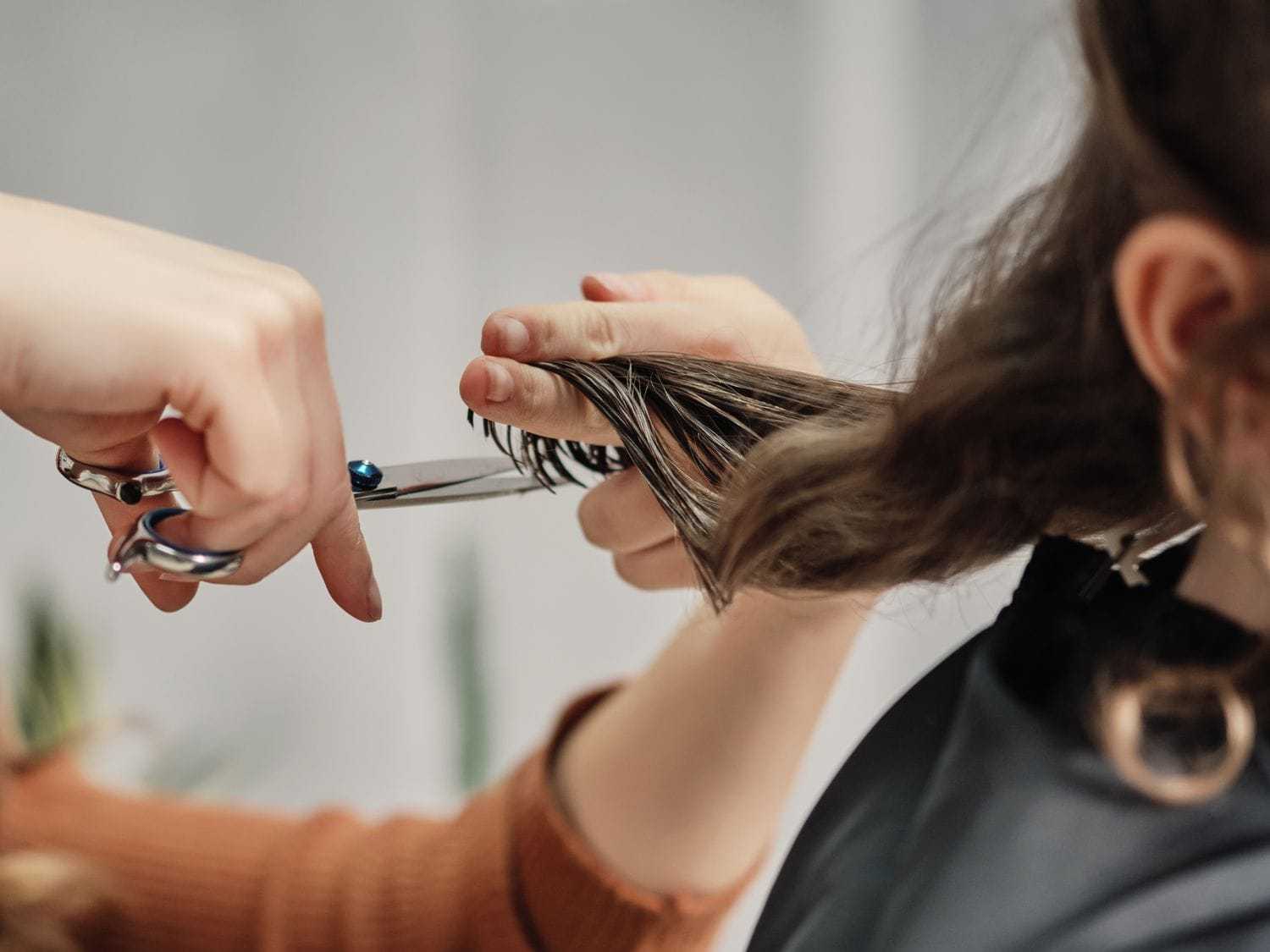 Hairdresser cutting a client's brown hair with scissors in a salon.