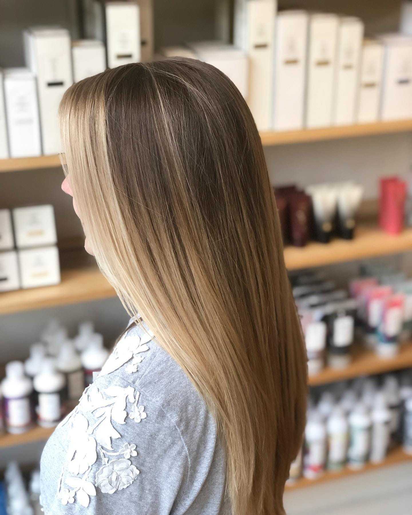 Woman with long, straight blonde hair in a salon surrounded by hair products.