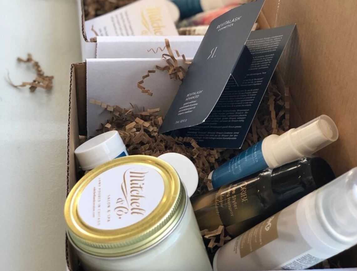 Gift box with candles, creams, and skincare products on shredded paper lining.