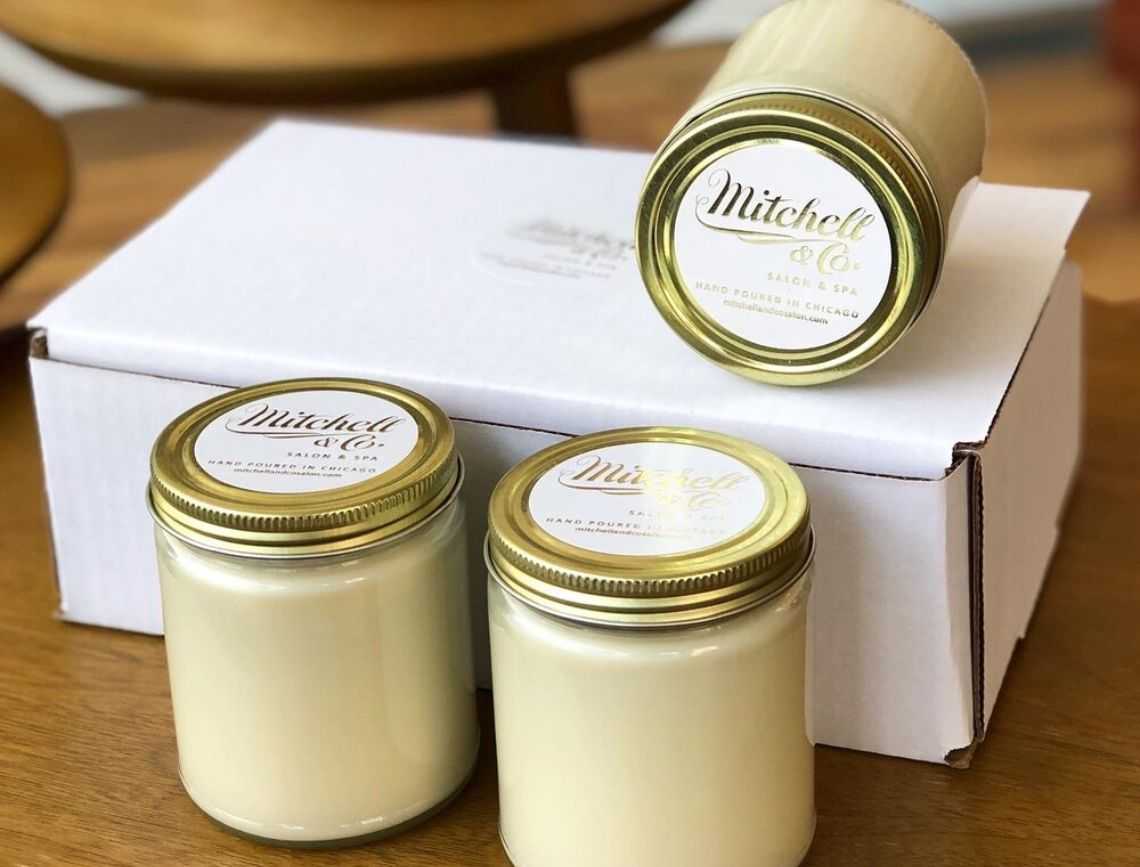 Jars of cream-colored candles with gold lids on a wooden surface.