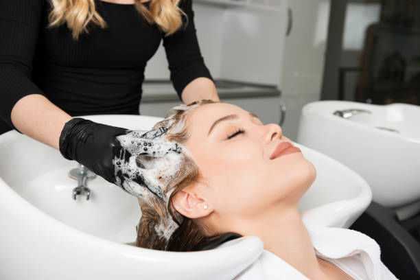 Woman enjoying hair wash in salon, stylist wearing gloves, white basin in background.