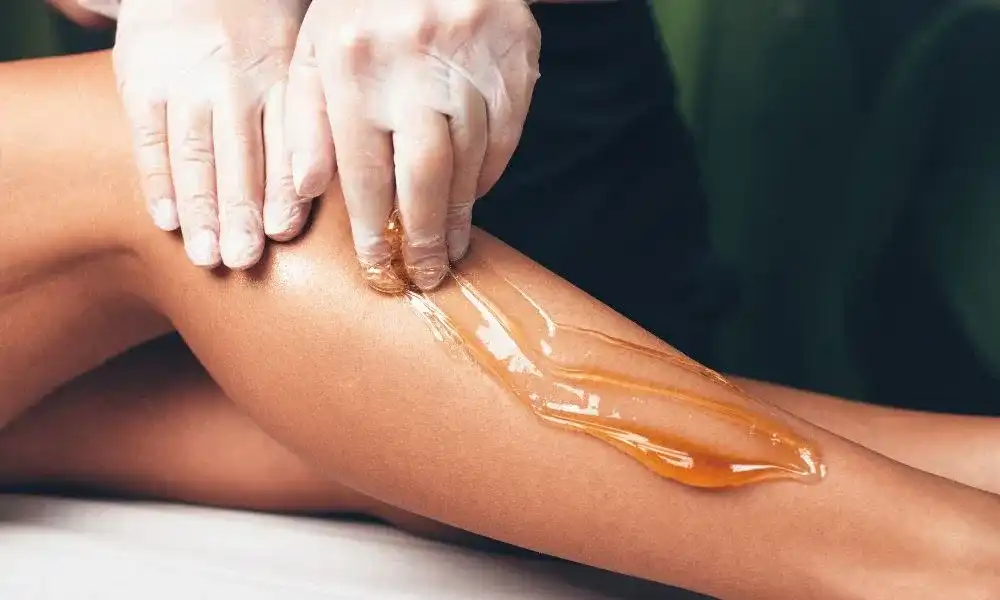 Leg hair removal using sugar wax applied with gloved hands.
