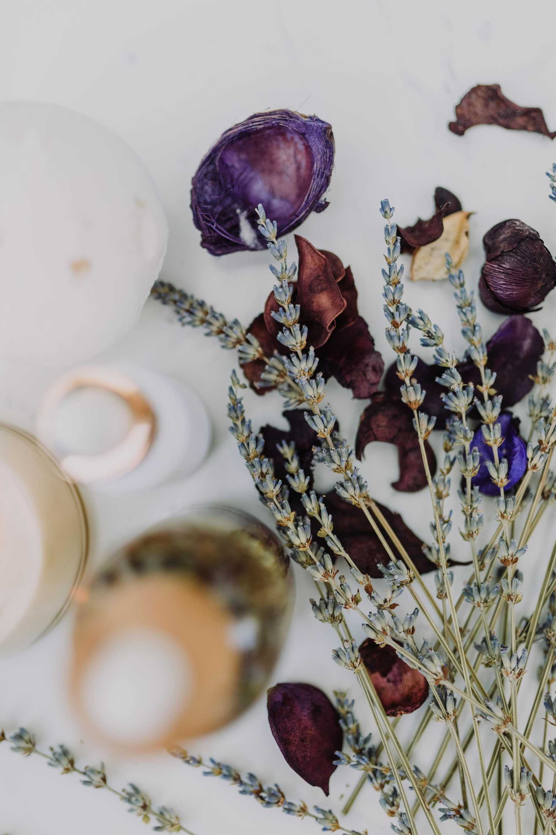 Dried lavender and purple petals arranged with white and amber bottles on a light surface.