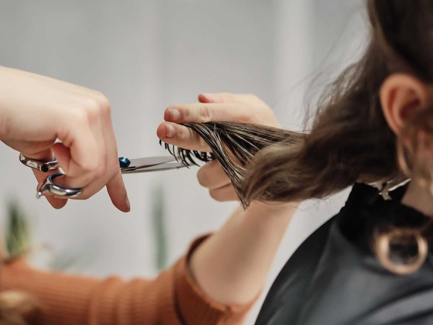 Hairdresser cutting a client's brown hair with scissors in a salon.